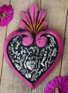 a pink and black heart sitting on top of a wooden table next to purple flowers