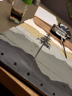 a wooden table topped with a painting and a cup filled with liquid next to it