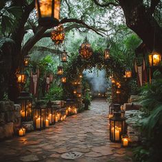 an outdoor walkway with lanterns and candles lit up in the night time, surrounded by greenery