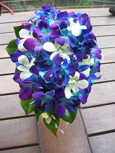 a bouquet of purple and white flowers in a vase on a wooden table with a person walking by