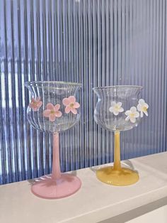 two glass vases sitting on top of a white table next to each other with flowers in them