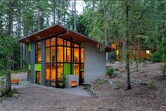 a green and gray house surrounded by trees in the woods at night with lights on