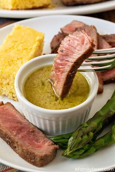 a plate with steak, asparagus and cornbread on it is being held by a fork