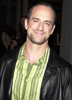 a man wearing a green striped shirt and black leather jacket smiles at the camera while standing in front of a group of people