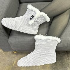 a pair of white knitted boots sitting on top of a gray couch next to a person's leg