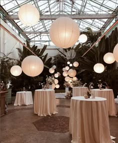 a room filled with lots of tables covered in white tablecloths and paper lanterns hanging from the ceiling