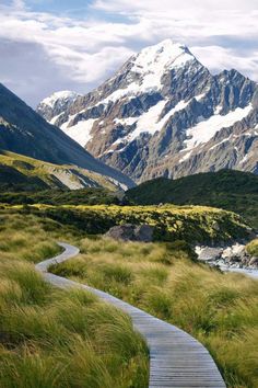 a wooden path leading to the top of a mountain with snow capped mountains in the background