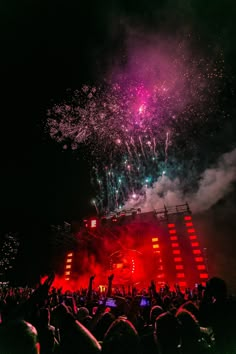 fireworks are lit up in the night sky above a crowd at an outdoor concert with people watching