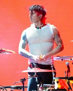 a man with tattoos on his arm standing in front of drums