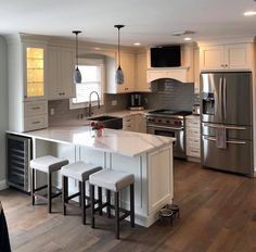 a large kitchen with an island and stainless steel appliances in the center, along with three stools