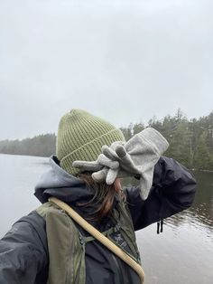 a person standing in front of a body of water wearing a green hat and jacket