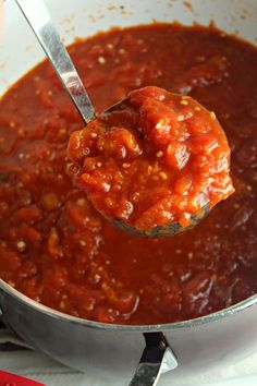 a ladle full of tomato sauce being held by a spoon over a pot filled with it