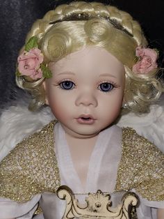 a close up of a doll with blonde hair and blue eyes wearing a white dress