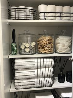 the shelves are filled with white towels and other bathroom items in glass containers on top of them