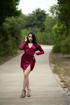 a woman in a red dress is talking on her cell phone while walking down a path