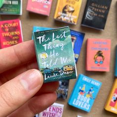 a hand holding a tiny book in front of a wall of small books on the floor