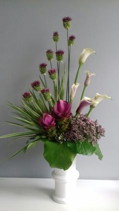 a white vase filled with purple flowers and greenery