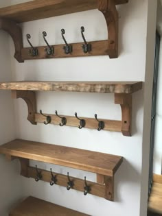 three wooden shelves with hooks on them in a room that has white walls and wood flooring