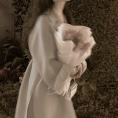 a woman wearing a white dress standing in front of a wall with ivy growing on it