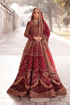 a woman in a red and gold bridal gown standing on a brick walkway with trees behind her