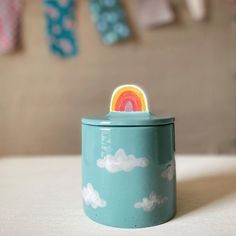 a blue canister with a rainbow painted on the top and clouds in the background