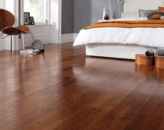 a bed room with a neatly made bed and hard wood flooring next to a window