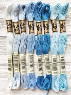 six skeins of blue and white yarn are lined up on a wooden surface