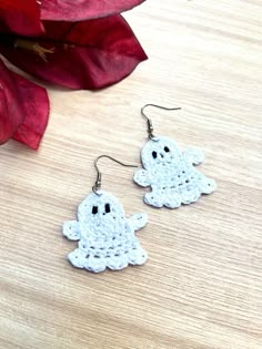 two crocheted ghost earrings sitting on top of a wooden table next to a red flower