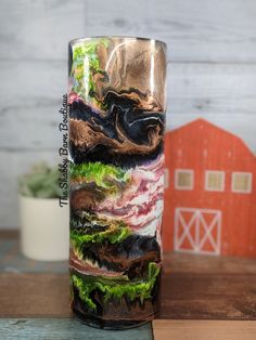 a tall glass sitting on top of a wooden table next to a red barn and tree