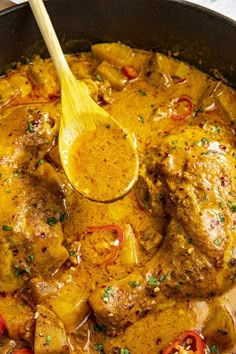 a pan filled with meat and vegetables covered in gravy next to a wooden spoon