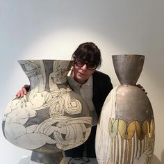 a woman standing next to two large vases on top of a white countertop