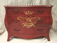 a red dresser with a checkered top and gold painted bee on the bottom drawer