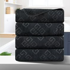 three black towels stacked on top of each other in front of a sink and window