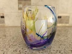 a colorful glass candle holder sitting on top of a marble counter next to a tiled wall