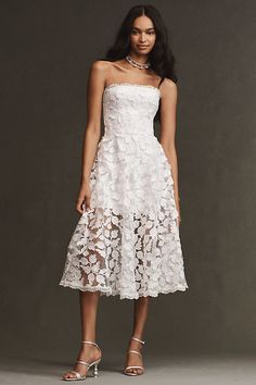 a woman is wearing a white dress with flowers on the skirt and high heeled sandals