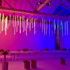 a room filled with tables and chairs covered in purple lights, hanging from the ceiling