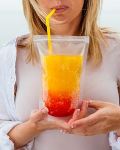 a woman holding a plastic cup filled with orange and yellow liquid