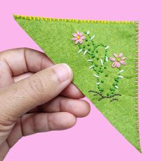 a hand is holding a green felt triangle with flowers on it and the bottom half has pink daisies