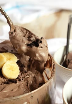 a bowl filled with chocolate ice cream and banana slices on top of it next to a spoon