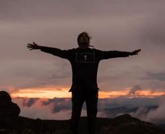 a man standing on top of a mountain with his arms outstretched