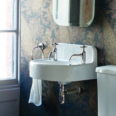 a white toilet sitting next to a bathroom sink under a mirror on a wall near a window