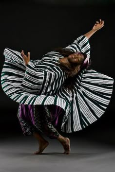 a woman is dancing with her arms spread out in front of her, wearing a striped dress