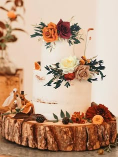 a white wedding cake decorated with flowers and greenery sits on a wooden slice in front of a mirror