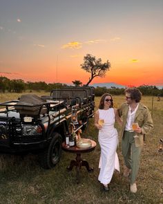 a man and woman standing next to a pick up truck with drinks in it at sunset