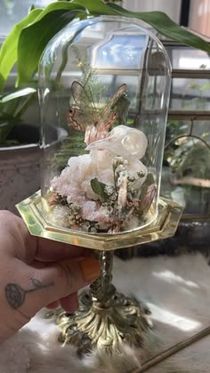 a person holding up a glass dome with flowers in it