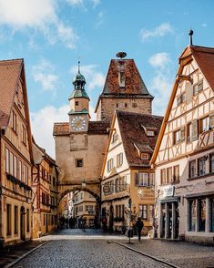 a cobblestone street with old buildings and a clock tower in the distance on a sunny day