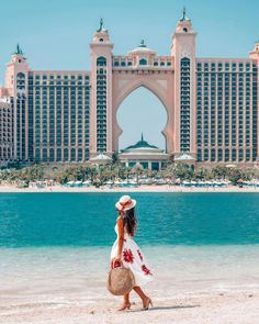 a woman walking on the beach in front of a large building with an arch over it