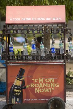 an old fashioned soda machine with lots of bottles on it's display stand in front of a tree