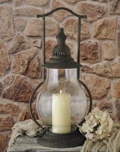 an old fashioned lantern with a lit candle on a table next to a stone wall