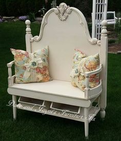 a white bench with two pillows on it in the grass next to a trellis